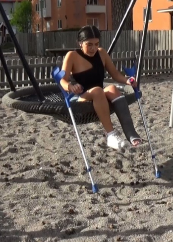 Pascale SLC #13 - In a parking lot we meet Pascale who has a black SLC on her left leg. She jumps up some stairs nearby and further into a playground where she jumps in the sand to a larger swing and speeds up the swing by using the crutches.