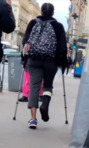 This girl broke her right ankle. She is wearing a SLC covered by a black sock. We see her on a bus. Then she gets off and goes on her crutches into the street, to get to another stop to get on another bus.